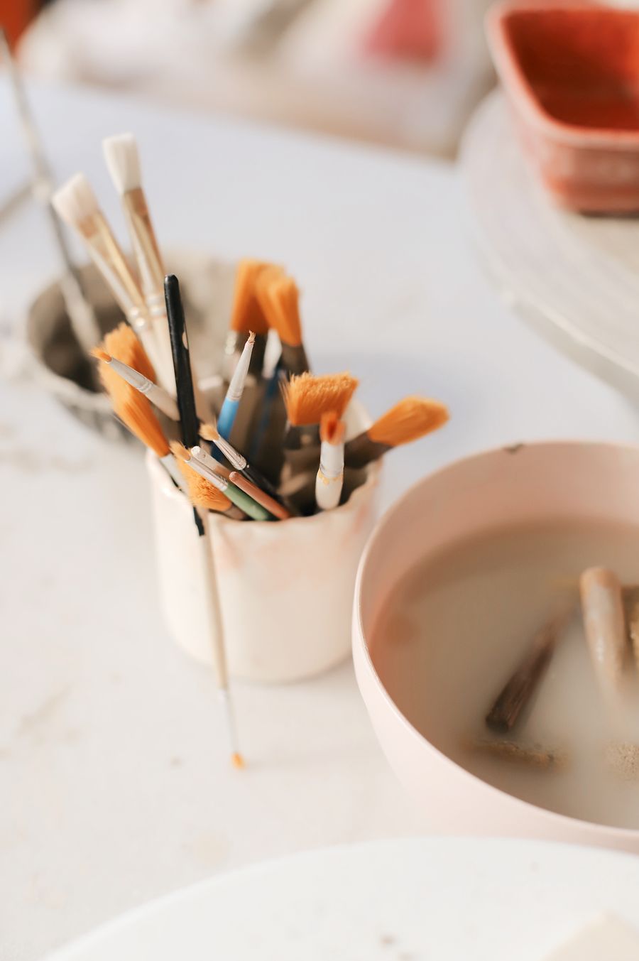 Close up of cups with paintbrushes and a bowl with water and clay — Thirty tools annotated figure