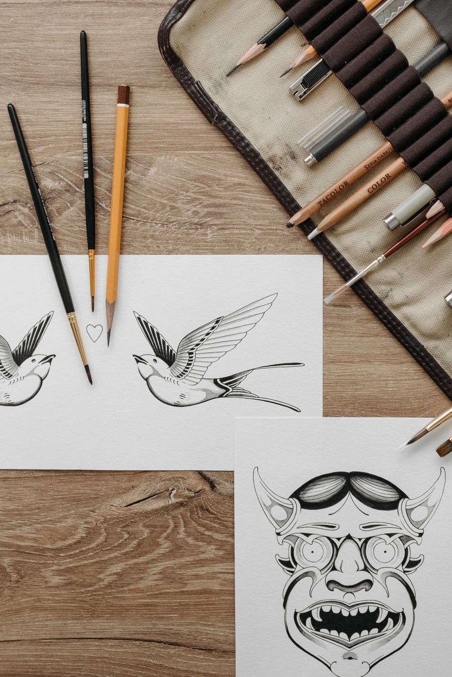 Sketches of tattoo design on paper beside drawing materials — Export a Design annotated figure